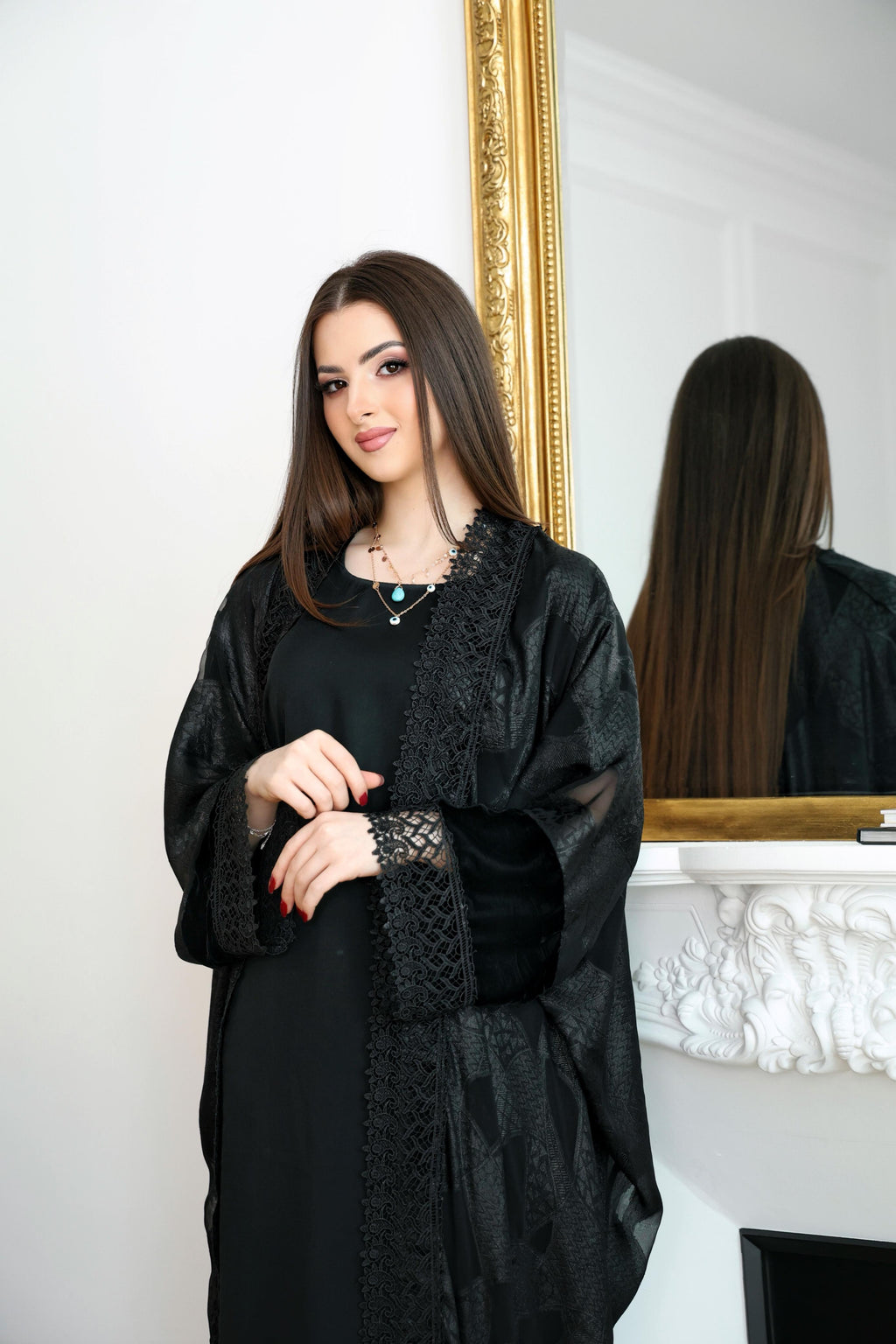 Woman wearing a black abaya with lace details in front of a mirror.Black abaya, classic black abaya, luxury abaya, elegant abaya, modest fashion, women’s abaya, Dubai abaya, designer abaya, Eid abaya, Ramadan abaya