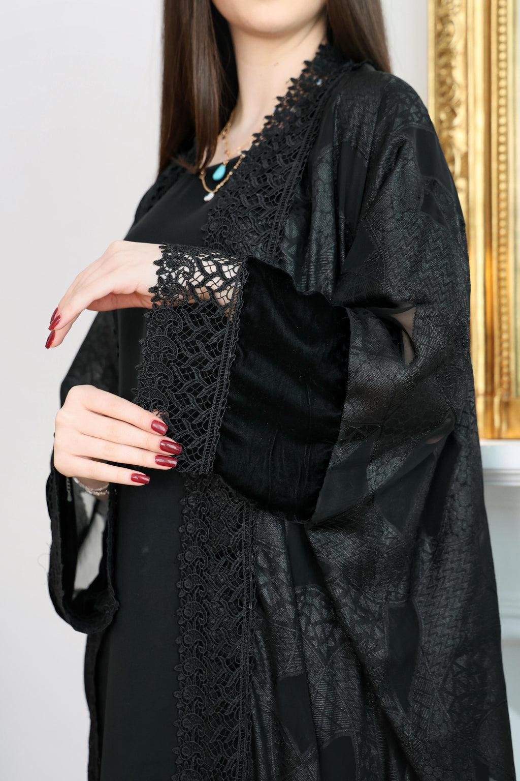 Woman wearing a black abaya with lace details in an indoor setting.Black abaya, classic black abaya, luxury abaya, elegant abaya, modest fashion, women’s abaya, Dubai abaya, designer abaya, Eid abaya, Ramadan abaya