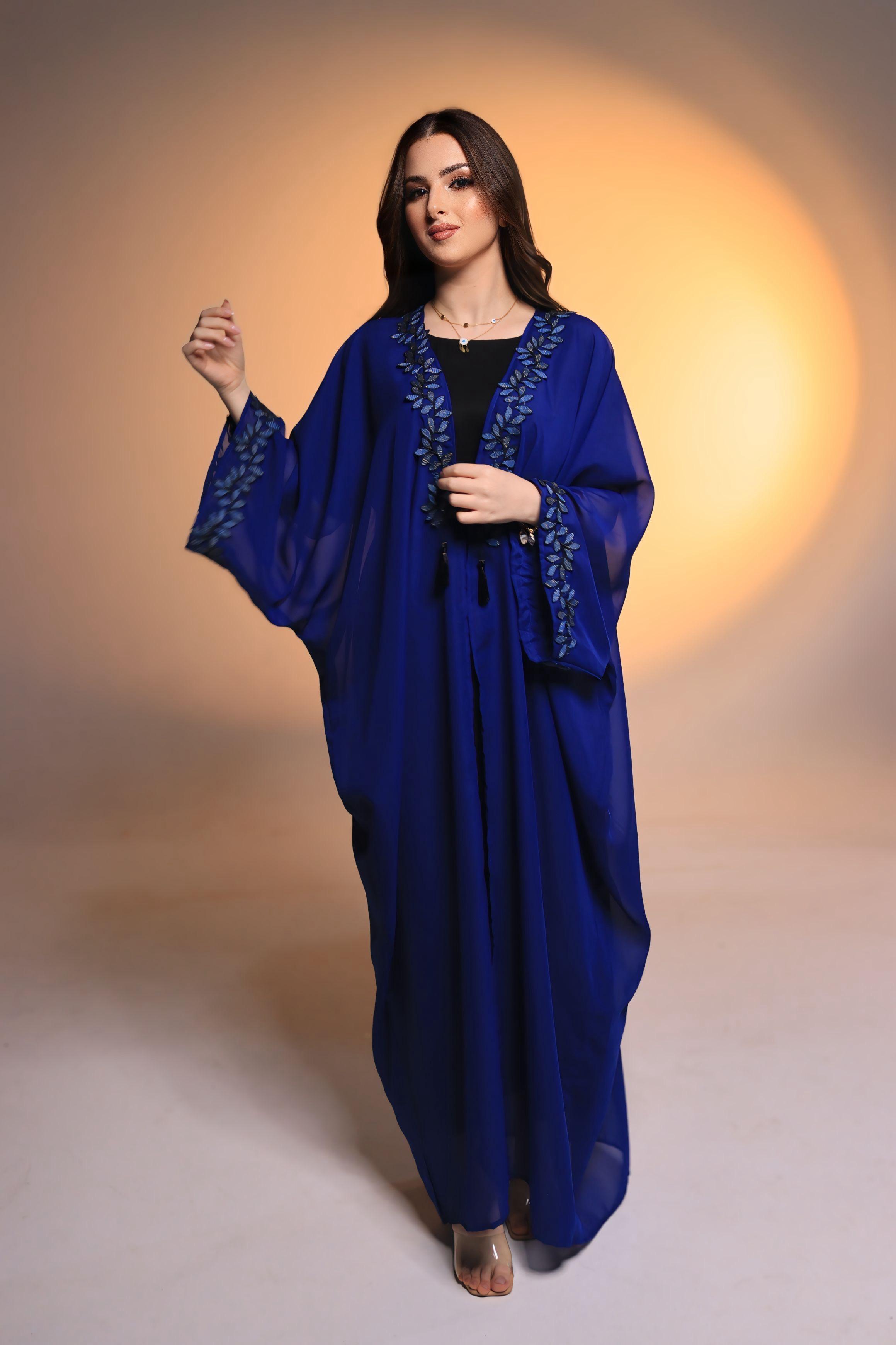 Woman wearing a blue abaya with intricate designs on a neutral background