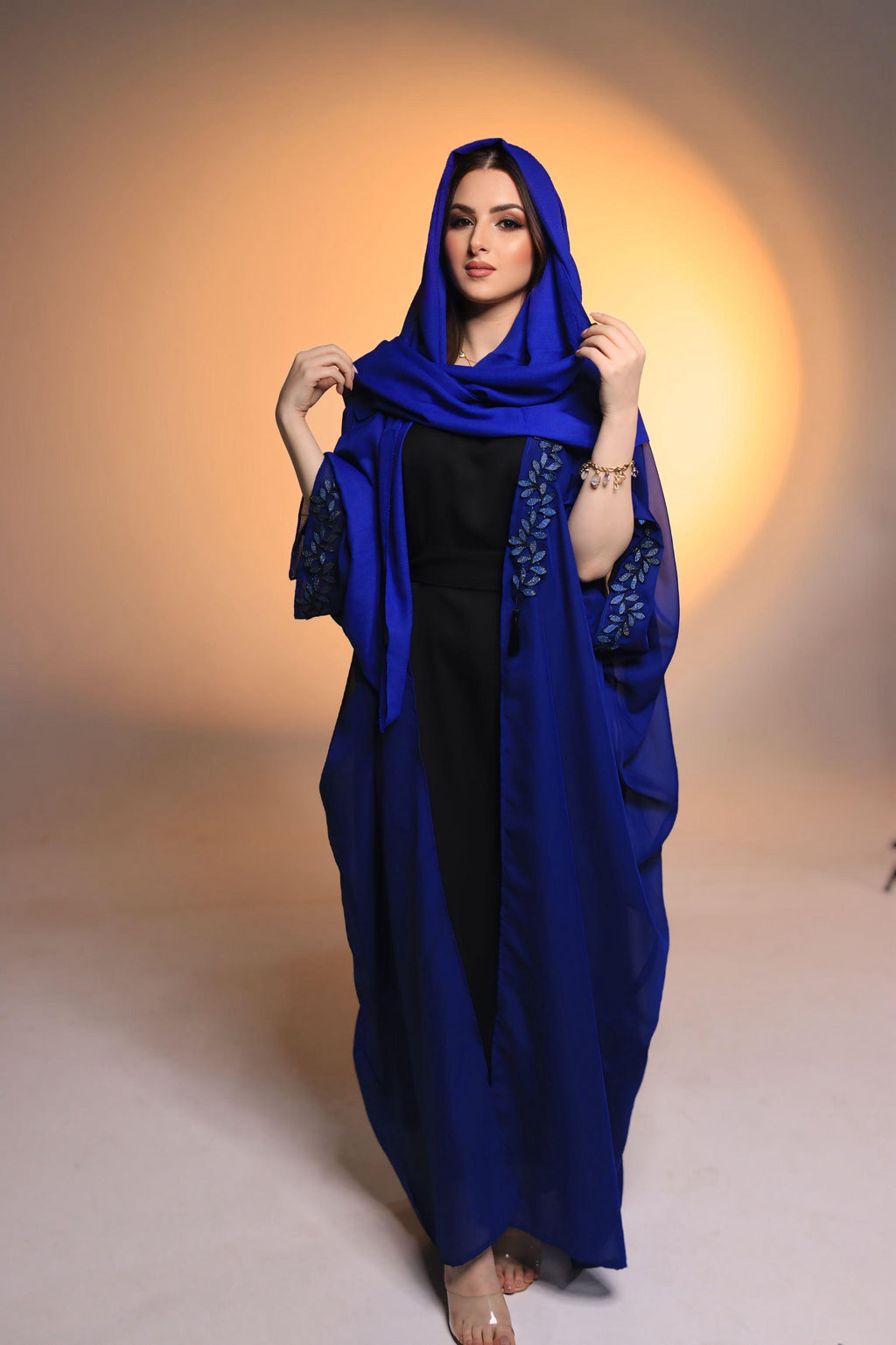 Woman wearing a blue abaya with a hood against a warm-toned background