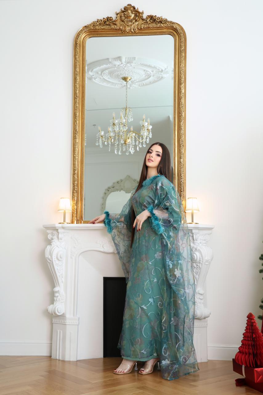 Woman in a teal dress standing in front of a large ornate mirror in an elegant Light blue abaya, sky blue abaya, elegant abaya, luxury abaya, minimalist abaya, modest fashion, Dubai abaya, Eid abaya, Ramadan abaya room.