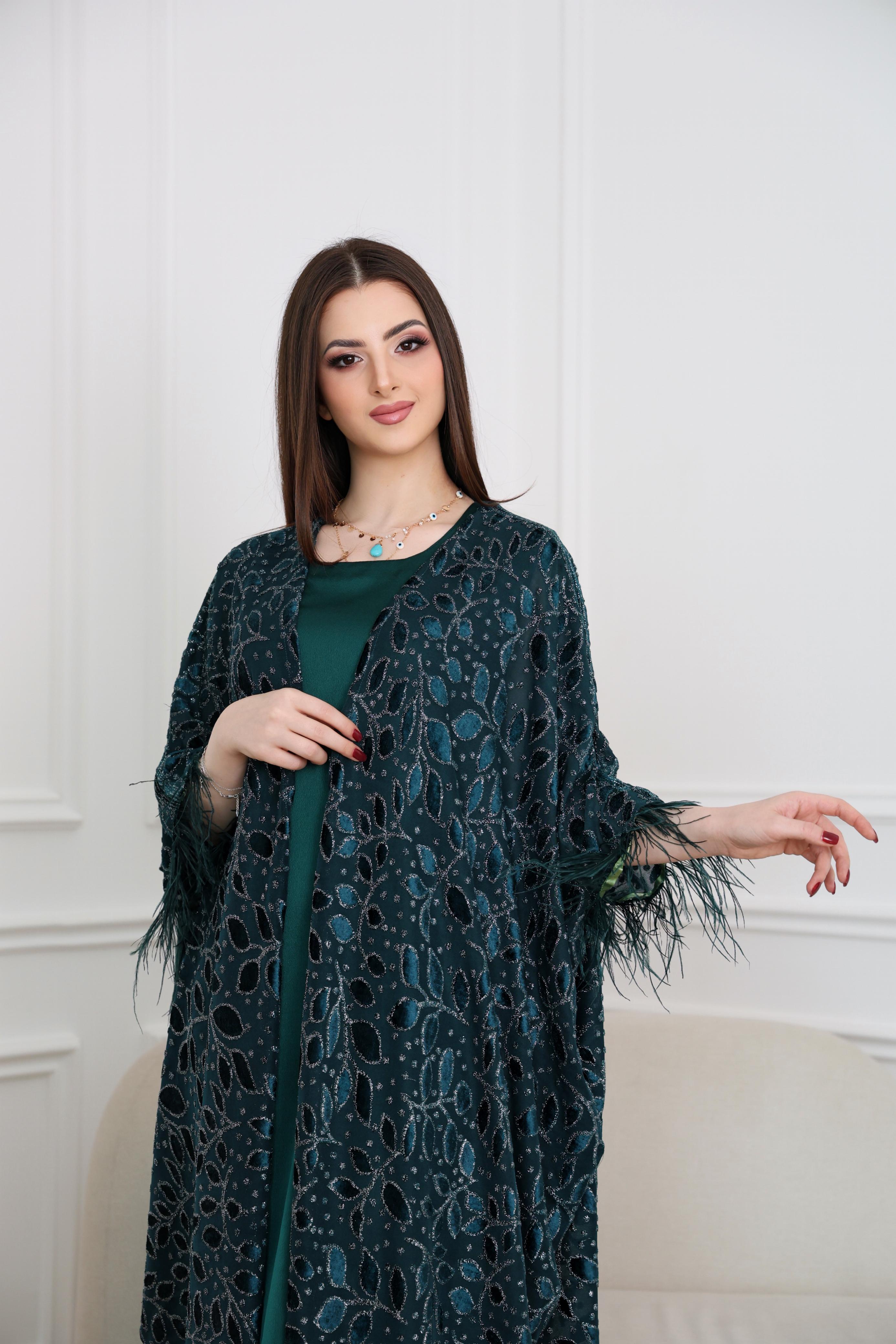 Woman wearing a dark green patterned coat over a green dress against a white background