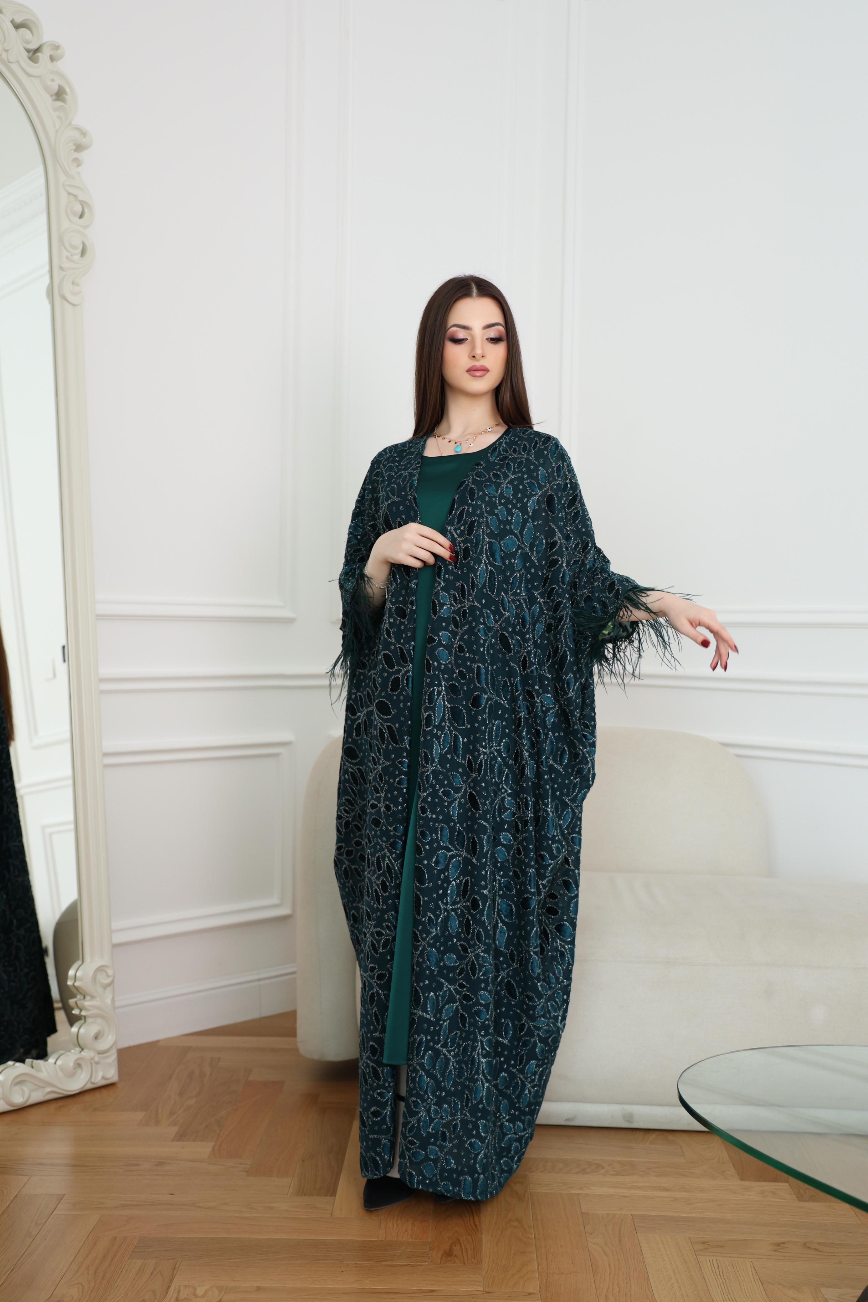 Woman wearing a dark green dress with floral patterns in a room with white walls and wooden floor.
