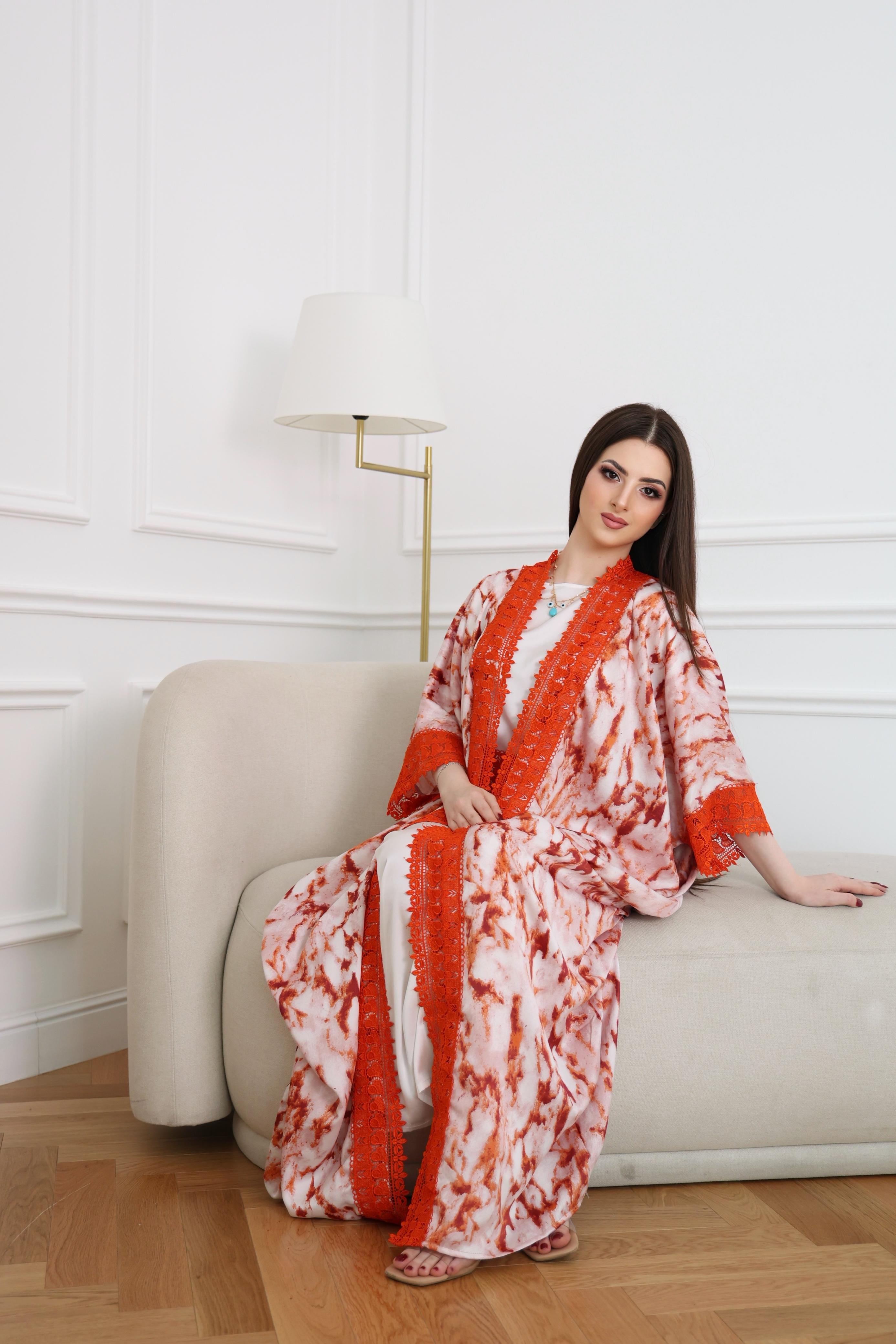 Woman in a red and white patterned dress sitting on a white couch against a white wall.