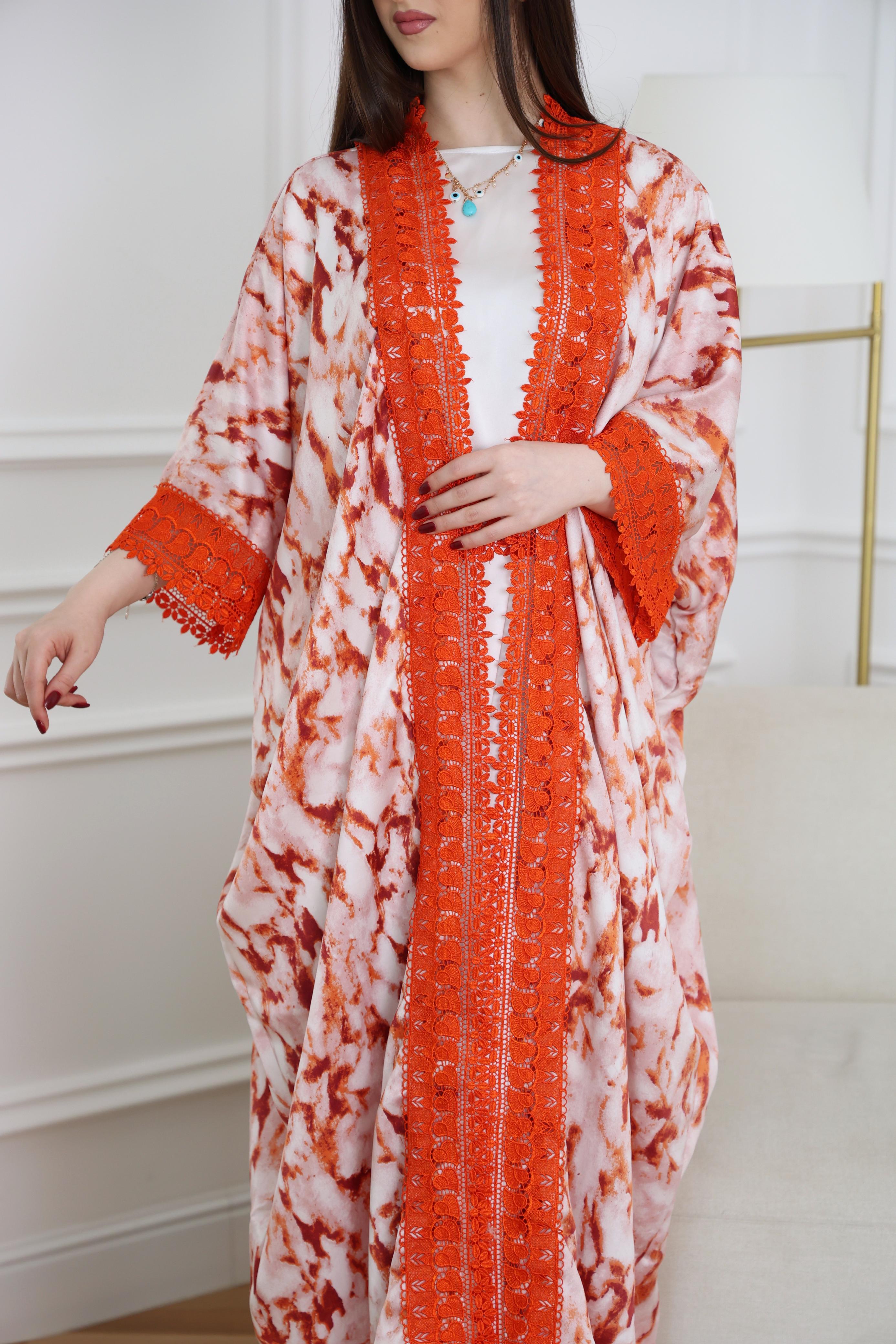 Woman wearing a long, patterned dress with orange and white design in a minimal indoor setting.