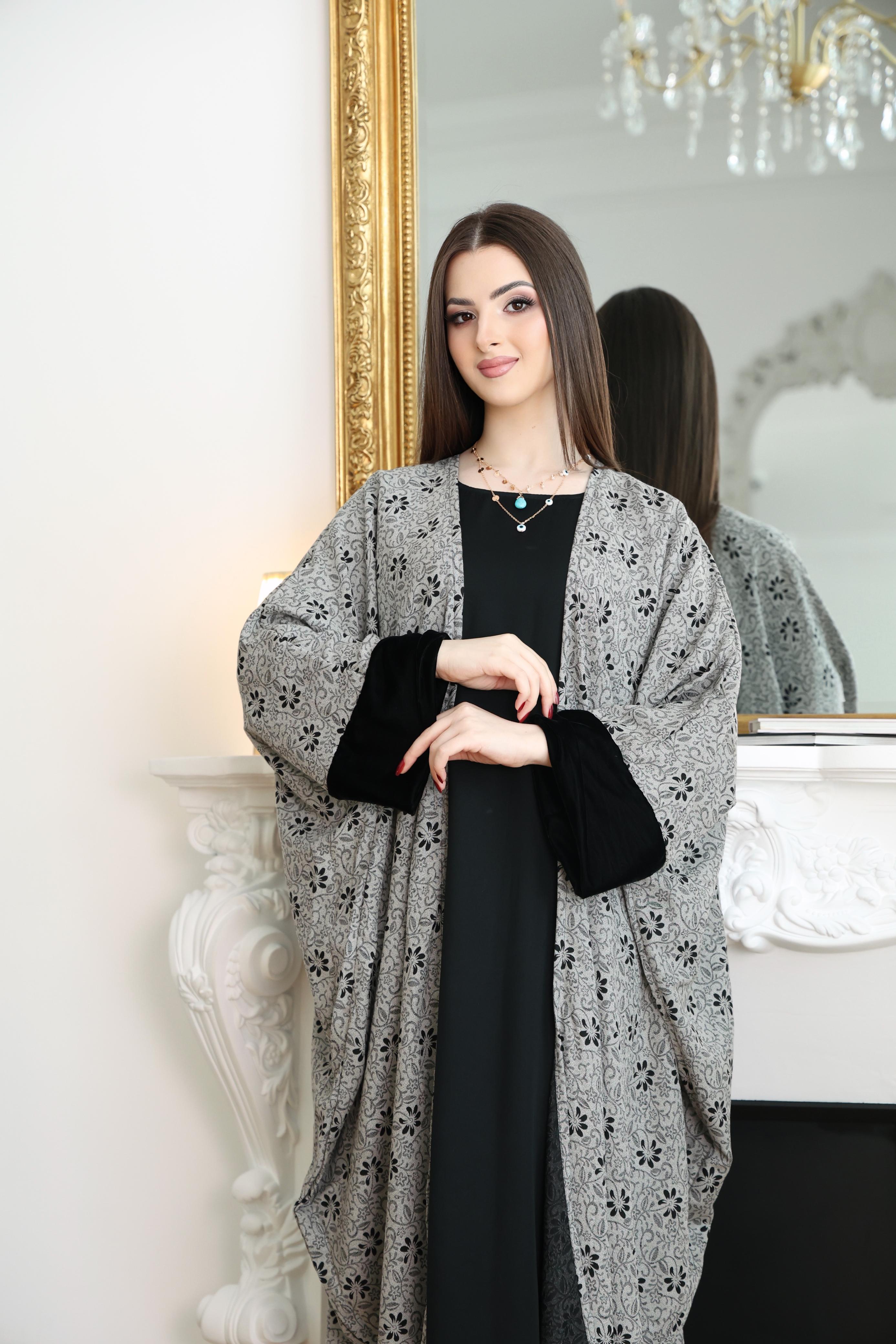 Woman wearing a gray floral kimono Abaya over a black dress in front of a mirror.
