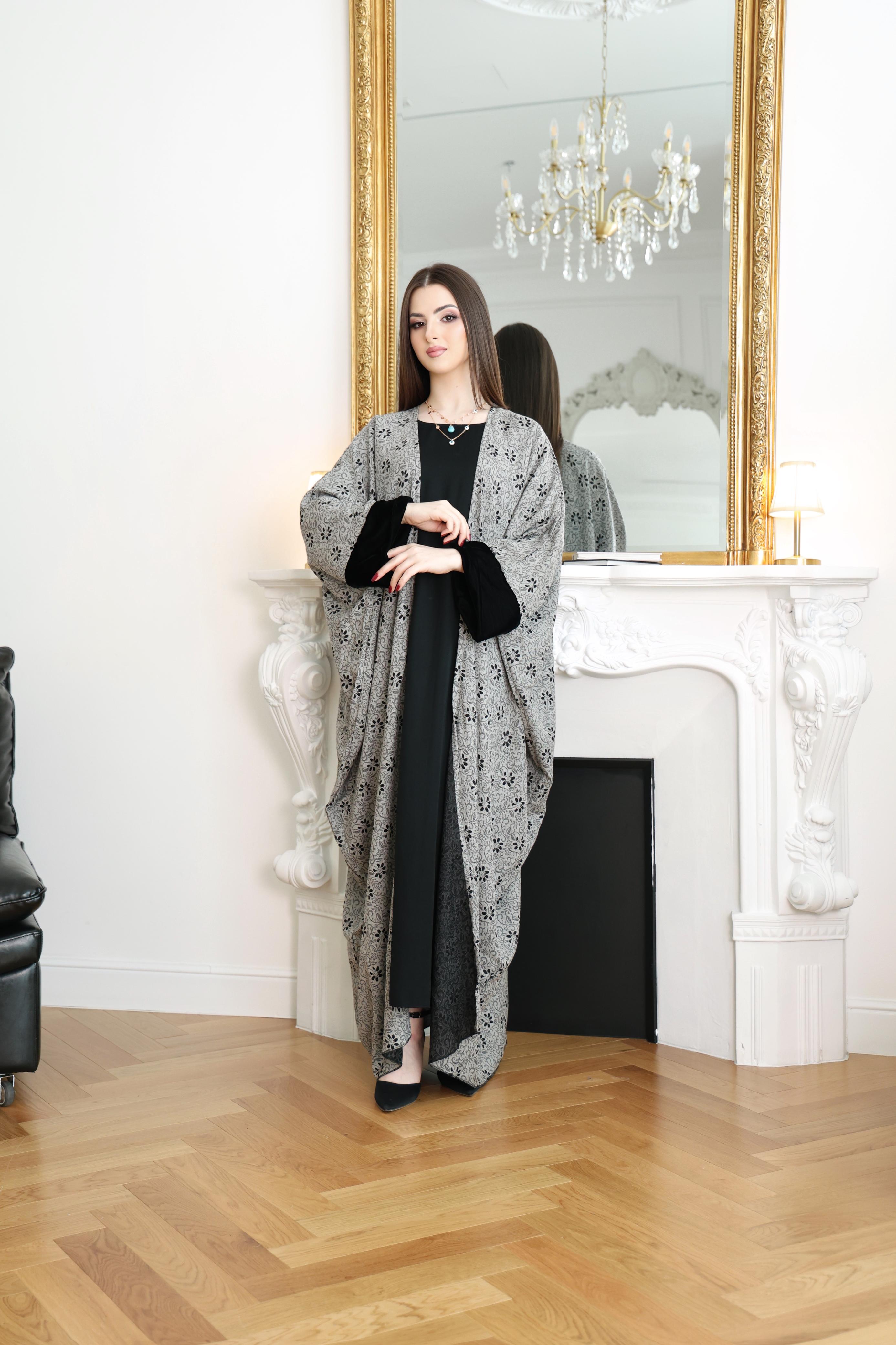 Woman in a gray patterned dress standing in a room with a mirror and chandelier.