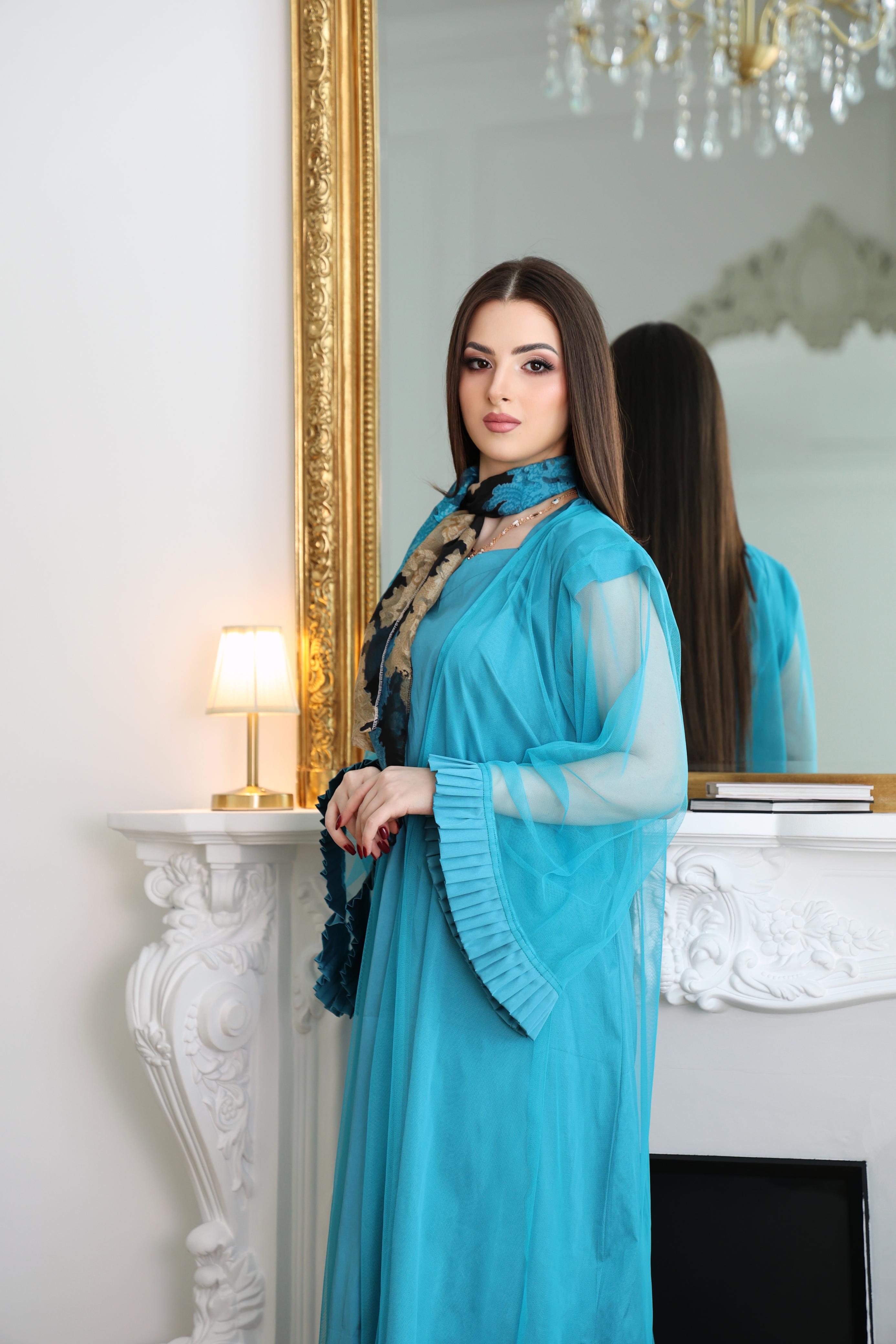 Woman in a blue abaya standing in front of a mirror in an elegant room.
