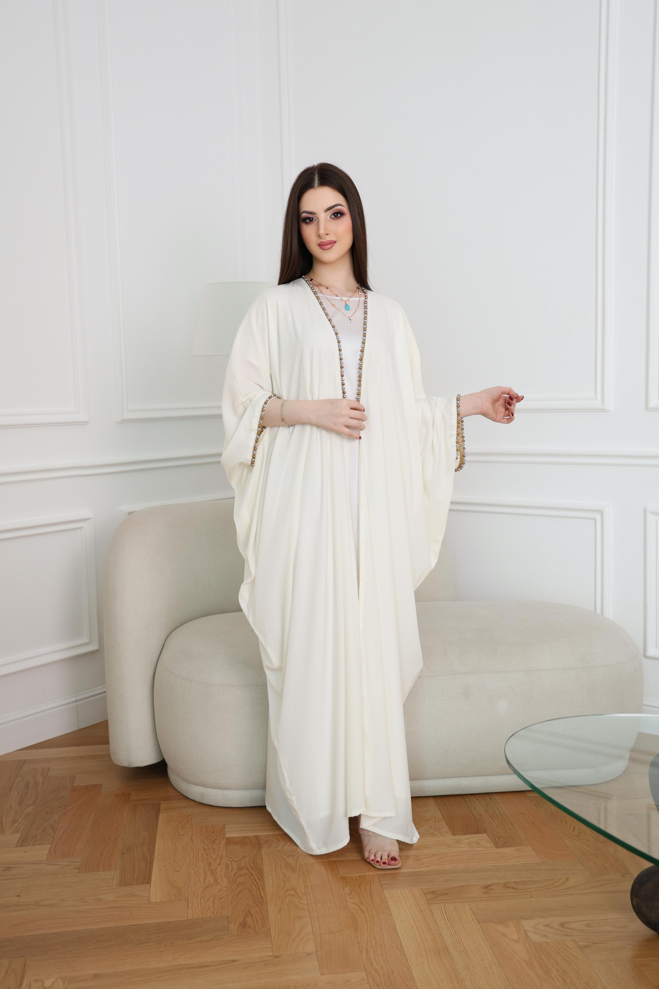 Woman in a white dress standing in a room with a white wall and wooden floor.